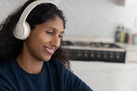 Indian woman listening with white headphones while relaxing in modern minimalist kitchen