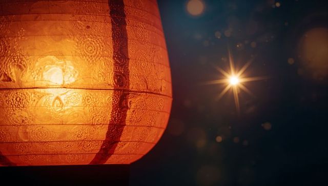 Glowing Orange Paper Lantern Against Night Sky with Lens Flare