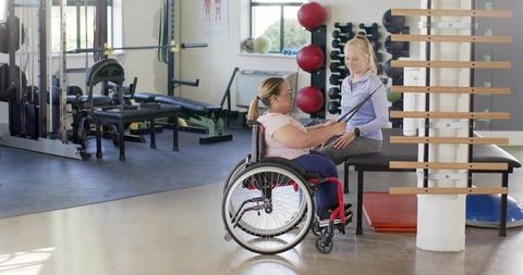 Rehabilitation therapist guiding wheelchair client using resistance band in inclusive gym