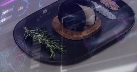 Minimalist black platter with glossy dome cheese on wood coaster, rosemary and flake salts