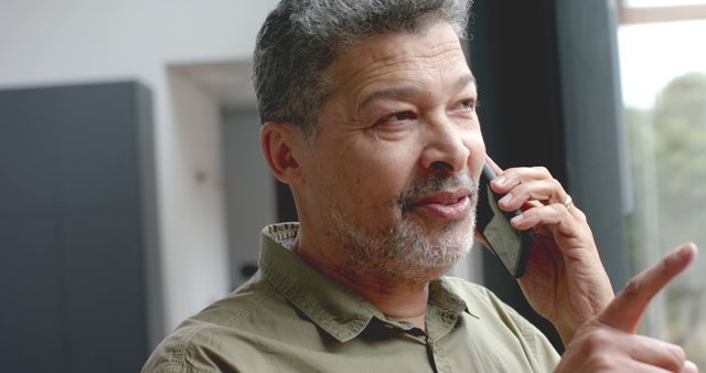 Middle-aged man speaking on a smartphone indoors, appearing engaged and relaxed. This can be used for communications, technology, mid-life demographics, and mature lifestyle-related content.