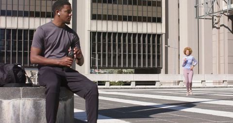 Urban Fitness Moment with African American Man Resting and Woman Jogging in Sunlit Plaza