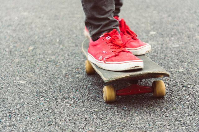 A person is skating on an asphalt surface, seen from the ankles down, displaying vibrant red sneakers. Useful for highlights on street sports, youth culture, fashion, and active lifestyle. Ideal for blogs, social media posts, and articles promoting urban activities and sneaker brands.