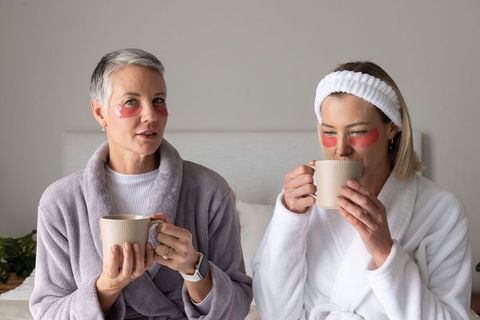 Cozy morning self-care ritual two women in robes wearing under-eye patches sipping mugs