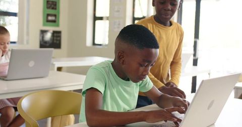 Black students collaborating on laptops in bright modern classroom with natural light