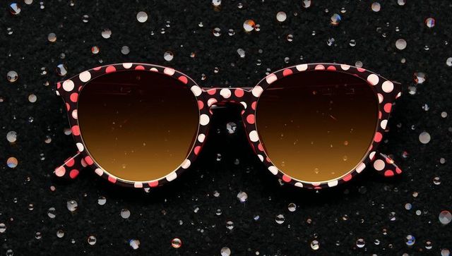 Resting polka-dot cat-eye sunglasses on black sequin fabric with brown gradient lenses