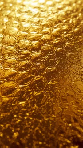 Vertical macro panning video showing golden honeycomb film texture with backlit droplets