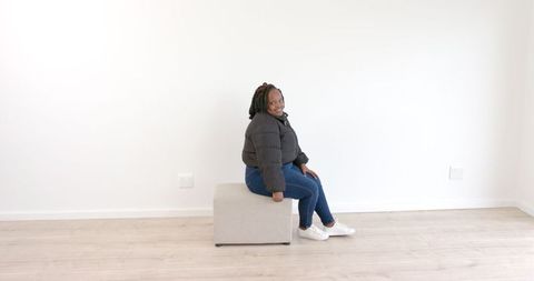 Person in Casual Outfit Sitting on Ottoman in Minimalist Room
