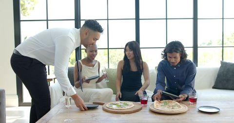 Young adults serving pizza and sharing drinks during casual living room gathering