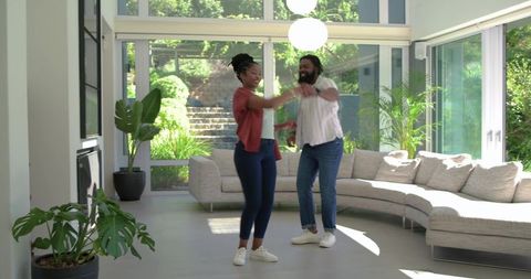 African american couple dancing in sunlit modern living room with curved sectional sofa