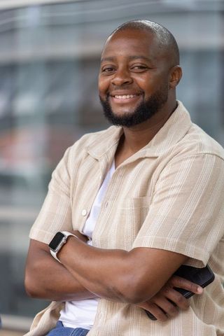 Confident smiling black man wearing beige shirt and smartwatch holding smartphone, urban