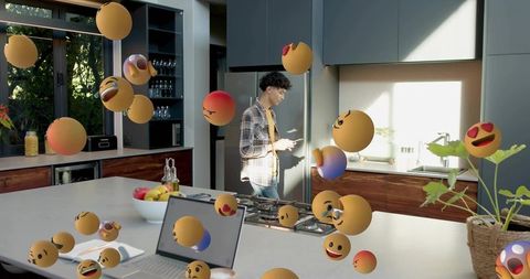 Young man checking smartphone in modern kitchen surrounded by floating emoji spheres