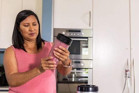 Indian woman preparing pink smoothie with personal blender at modern kitchen countertop