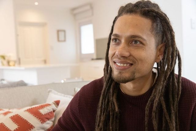 Smiling man with dreadlocks sitting on sofa in cozy open-plan living room