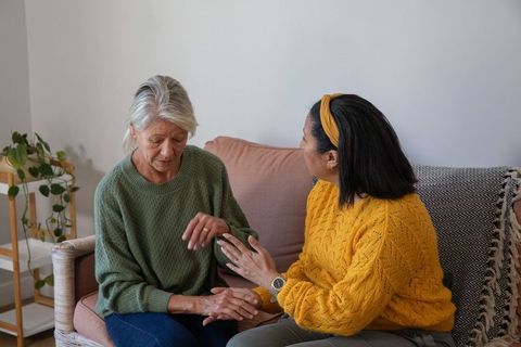 Senior women sharing support and holding hands on cozy sofa in warm home interior