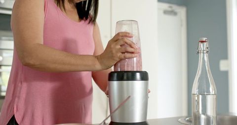 Mature woman blending pink smoothie in modern kitchen wearing pink sleeveless top