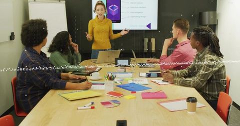 Woman in mustard sweater presenting to small team in meeting room for brainstorming session