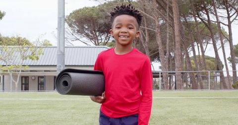 Youthful Boy Holding Exercise Mat on Outdoor Sports Field