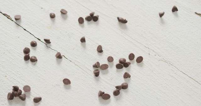 Delicious chocolate chips scattered on white wooden surface. Ideal for baking, dessert, food blog, or cafe decor.