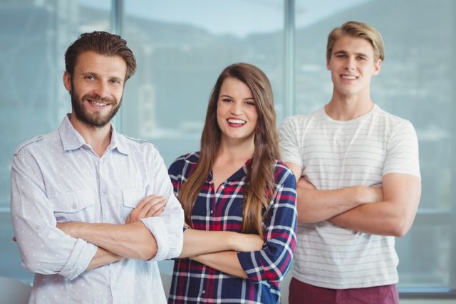 Three young professionals standing with arms crossed in a modern office, exuding confidence and teamwork. Ideal for use in business-related content, team-building materials, leadership articles, and workplace culture promotions.