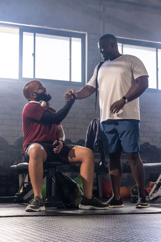 Supportive workout bonding: men clasping hands on gym bench celebrating strength and teamwork