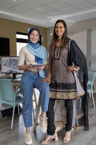 Collaborating diverse women in hijab and tunic reviewing tablet and architecture floor plan