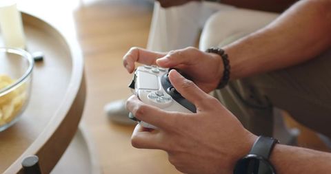 Hands holding silver-black game controller on lap near snack bowl in cozy living room