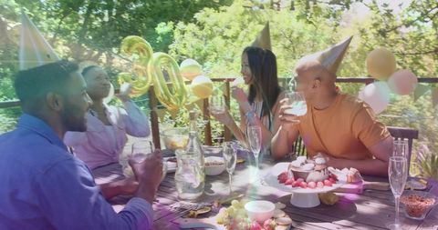 Friends toasting at 30th birthday on outdoor deck with cake and gold balloons