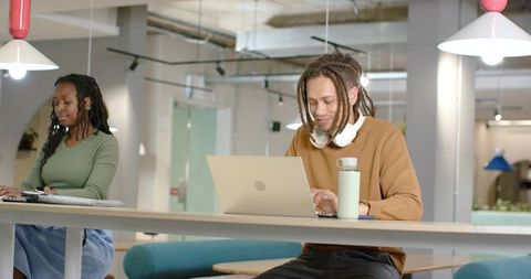 African American professionals collaborating at high coworking table with laptops, headphones