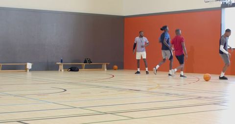 Indoor basketball team practicing dribbling and passing drills on gym court with coach