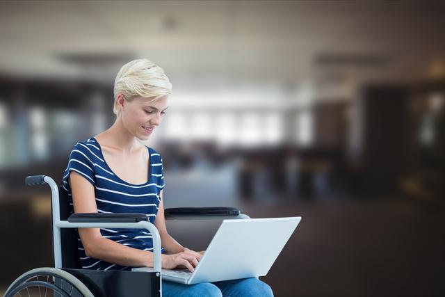 Digital composite of Businesswoman using laptop in wheelchair over blurred background