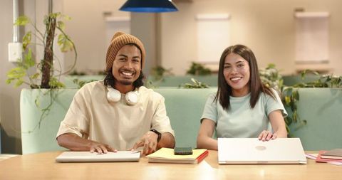 Smiling young peers collaborating and studying at modern coworking lounge with laptops