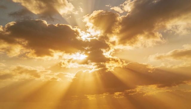 Golden sunrise rays piercing cloud bank casting warm crepuscular beams across sky