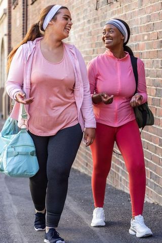 African american women walking laughing in pink activewear carrying gym bags urban wellness