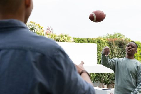 African american young male friends tossing football on backyard patio, casual outdoor game
