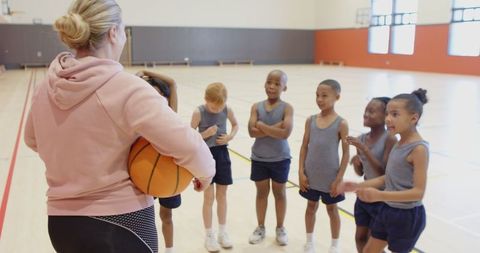 Diverse youth basketball team listening to coach in gym