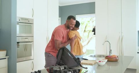 African american father and teenage son hugging in modern kitchen, family warmth