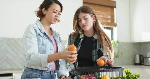 Diverse friends sorting fresh oranges at bright modern kitchen island for healthy living