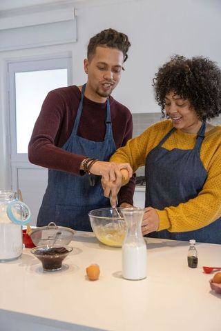 Young couple baking together at kitchen island whisking batter and cracking eggs for dessert