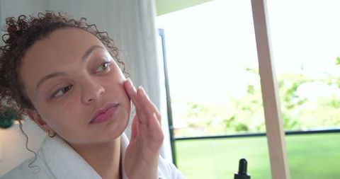 African woman applying facial serum on balcony during natural light skincare routine