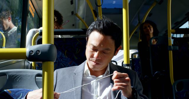 Depicts businessman in suit focused on disentangling earphones while commuting by public bus. Useful for illustrating urban transport, daily commute, multi-tasking during travel, and modern technology usage in transit.
