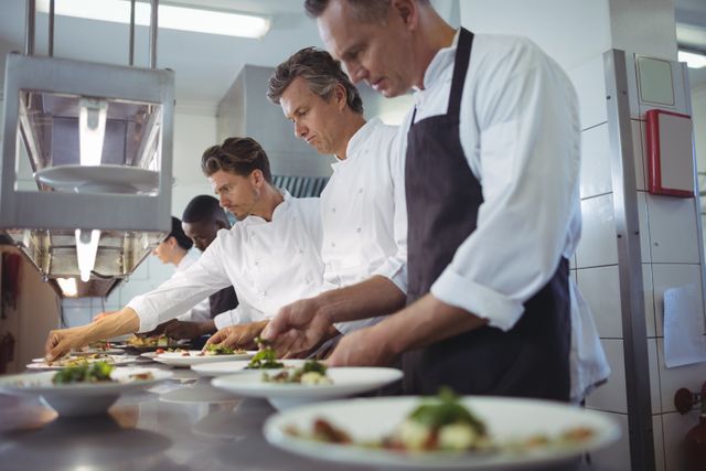 Team of chefs garnishing meal on counter in commercial kitchen
