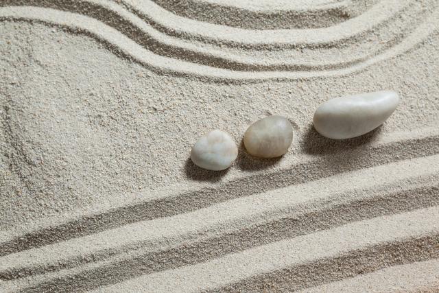 White pebble stones arranged on rippled sand creating a serene and balanced composition. Ideal for use in wellness and spa promotions, meditation and relaxation content, nature and minimalism themes, or as a calming background for various projects.