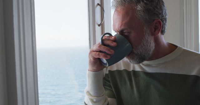 Middle-aged man enjoying hot drink at home with ocean view - Download Free Stock Images Pikwizard.com