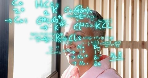 Mature woman researcher studying neon chemical formulas on glass at sunlit office window