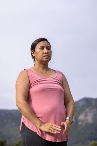 Mature asian woman meditating outdoors in mountain landscape wearing pink top
