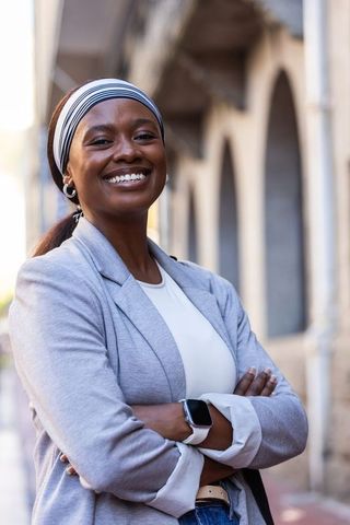 Confident african businesswoman standing with arms crossed smiling in sunlit urban arches