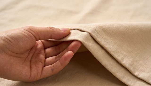 Male hand lifting beige cotton fabric revealing woven hem closeup texture detail textile