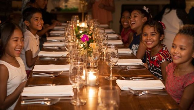 Children smiling and celebrating dinner at candlelit long table in cozy restaurant