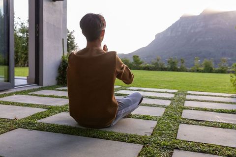 Young person meditating on patio with concrete pavers and mountain ridge sunrise